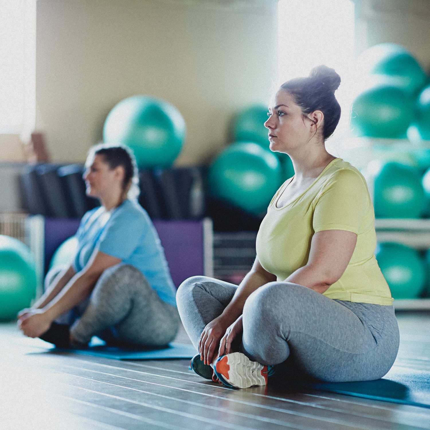 Two overweight women sitting with crossed legs on mats and getting ready for next exercise